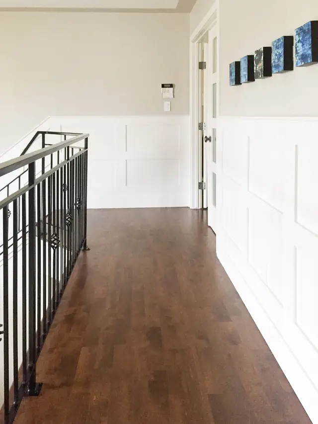 Stair landing with white wainscoting, an iron railing and hardwood floors
