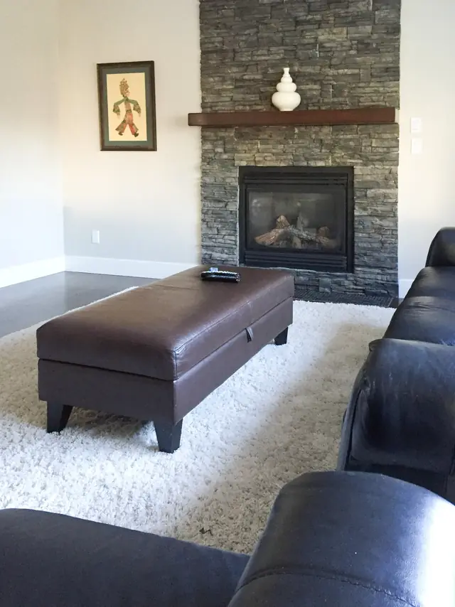 Living room with a stacked stone fireplace and a leather ottoman