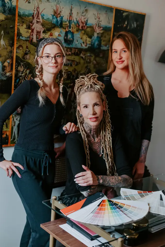 Amanda and two painters in black holding open fan decks of paint swatches in front of a large painted artwork