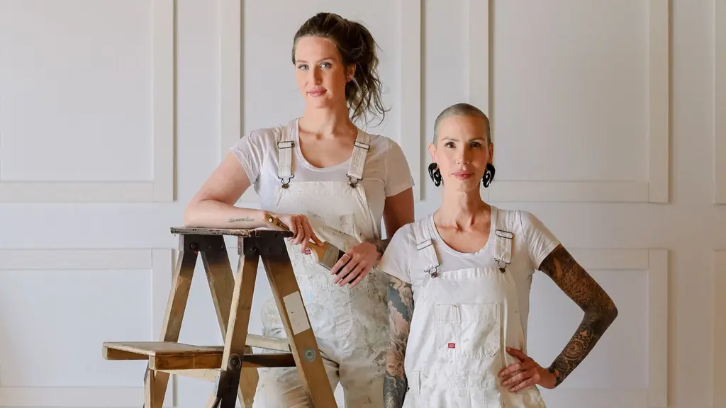 Two painters in white overalls beside a wooden step ladder against a panelled white wall
