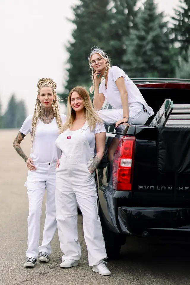Three painters in white overalls on and beside a black pickup truck, trees behind